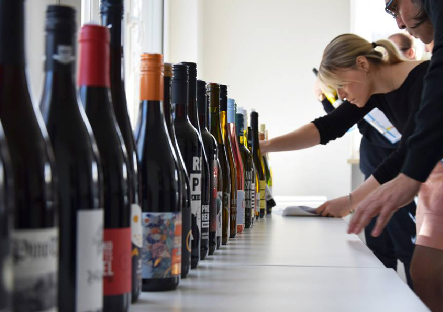 a line up of wine bottles with inspectors looking at the labels